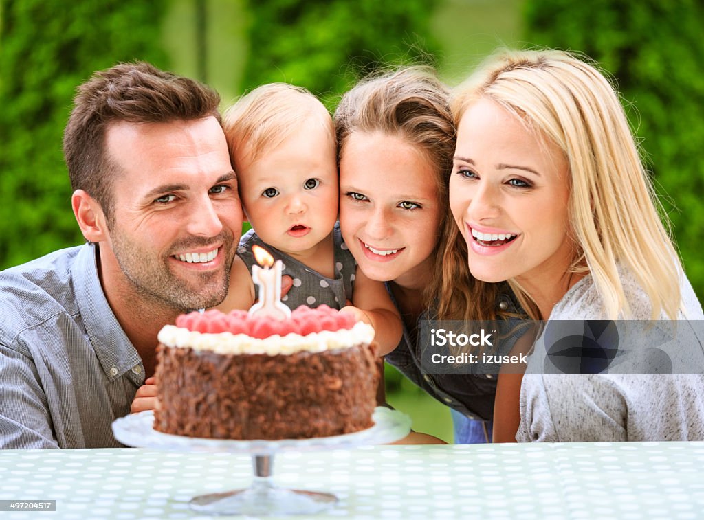 Family celebrating first birthday Outdoor portrait of happy family celebrating firts birthday their cute baby girl. Everyone looking at birthday cake.  12-23 Months Stock Photo