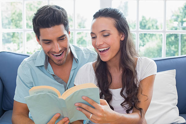 Couple laugh as they read book on the couch