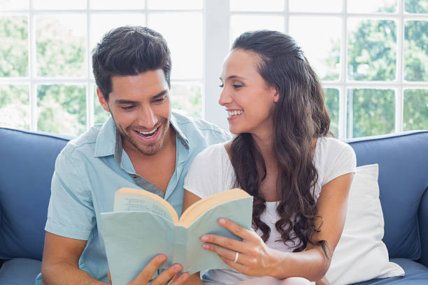 istock Couple smile as they read book on the couch 497209547