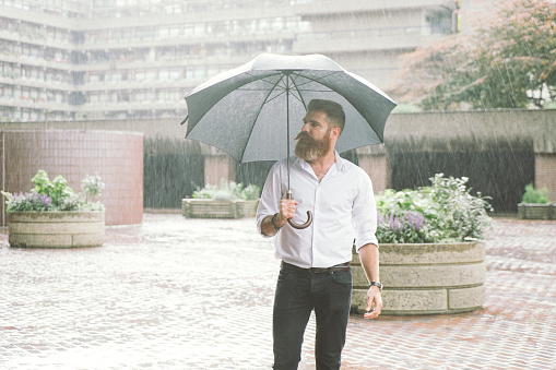 Young Latino from Bogota Colombia between 20 and 29 years old waits for his Uber in the street while it rains and uses his umbrella on a rainy afternoon