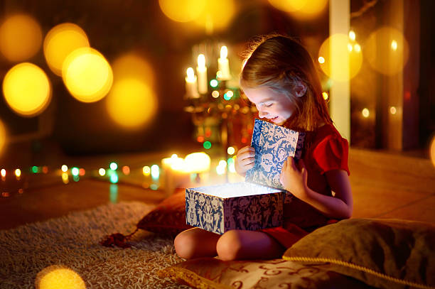 Little girl opening a magical Christmas gift Adorable little girl opening a magical Christmas gift by a Christmas tree in cozy living room in winter magical equipment stock pictures, royalty-free photos & images
