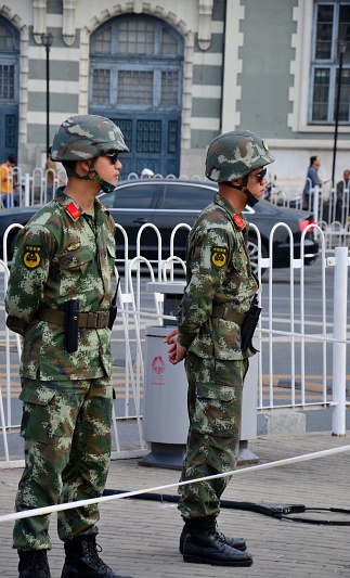 Beijing, China - October 18, 2015: Two uniformed Chinese soldiers of the People's Liberation Army man a checkpoint at the edges of Beijing's famous Tiananmen Square. The soldiers wear full camouflage kids and battle helmets. 