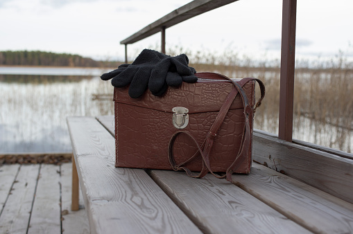Retro looking leather bag with woolen gloves on it laid on the pier, concept of travel