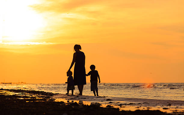 istock mother and two kids walking on beach at sunset 497218342