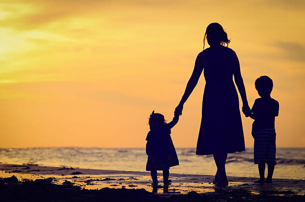 istock mother and two kids walking on beach at sunset 497218384