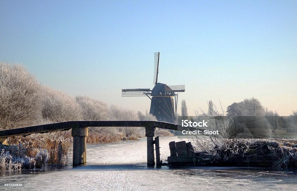 Dutch winter landscape with frozen canal and windmill Typical Dutch winter landscape with traditional windmill and frozen canal, bordered by frost-covered trees on a clear and sunny day in winter. 2015 Stock Photo