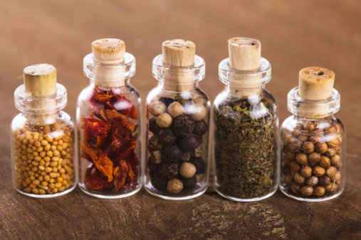 Little souvenir bottles with spices over wooden table. Mustard, paprika petals, peppercorns, basil, coriander