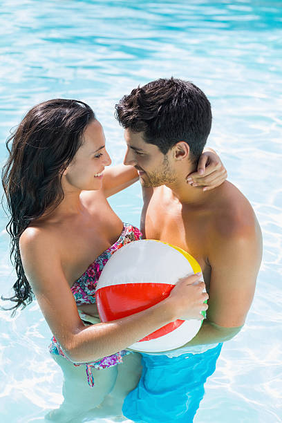 casal abraço, enquanto joga com bola de praia - swimming trunks women beach ball couple - fotografias e filmes do acervo