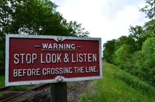 A sign next to a pedestrian crossing over a rural Southern England railway line warning that care should be taken.