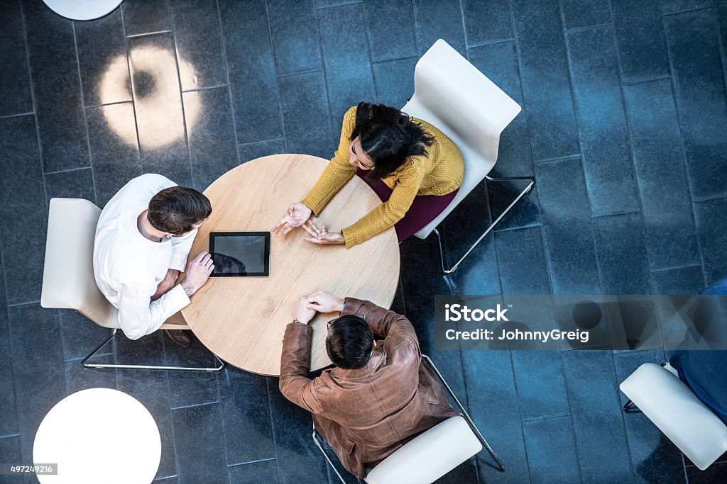 Business people meeting in modern office, view from above Small group of corporate business people at round desk using digital tablet. Colleagues discussing business together overhead view. Circle Stock Photo