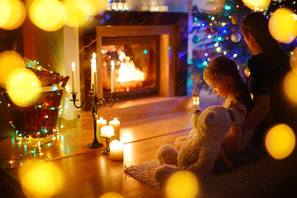 istock Young mother and daughter sitting by a fireplace on Christmas 497251008