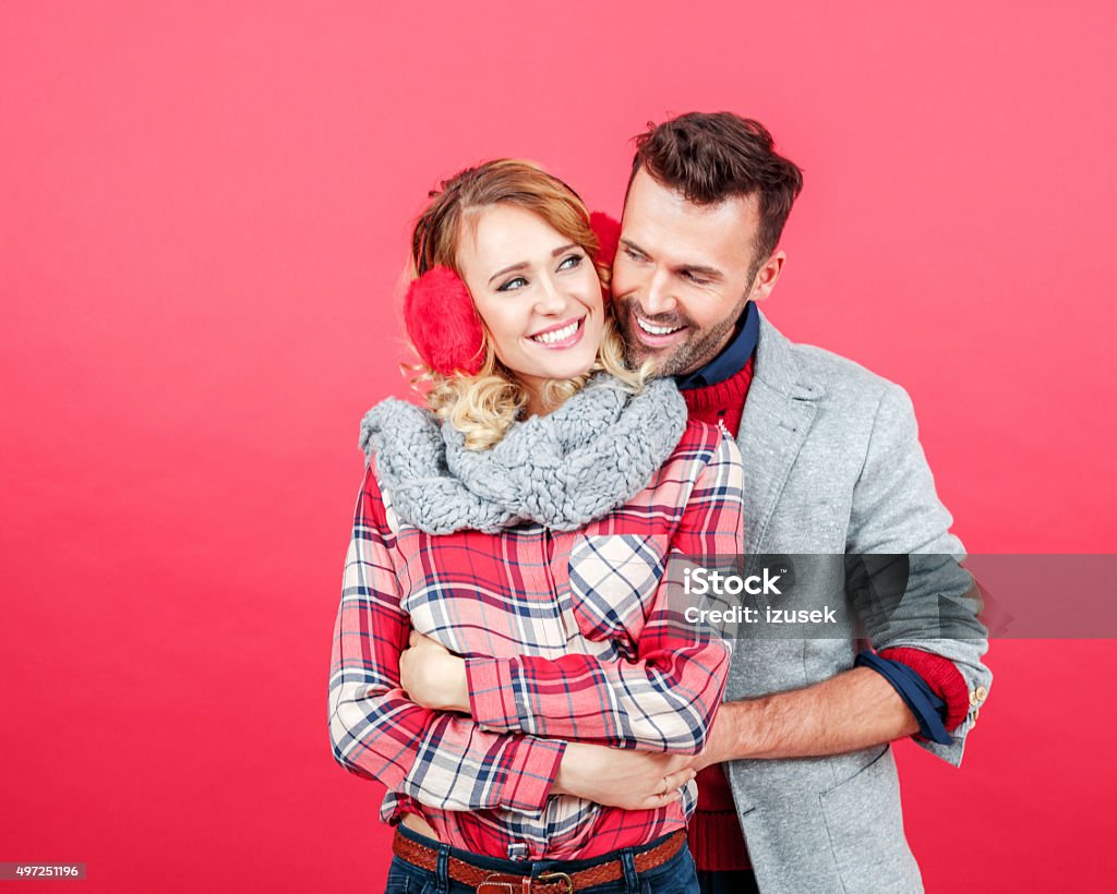 Happy couple in winter outfit against red background Studio portrait of happy, affactionate couple in winter outfits embracing against red background. Colored Background Stock Photo