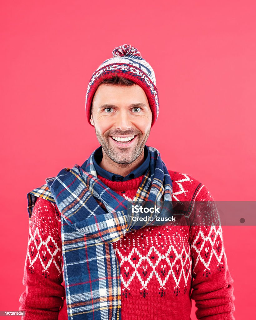 Happy man in winter outfit against red background Studio portrait of happy man in winter outfit - cap, scarf and sweater, standing against red background and laughing at camera. Men Stock Photo