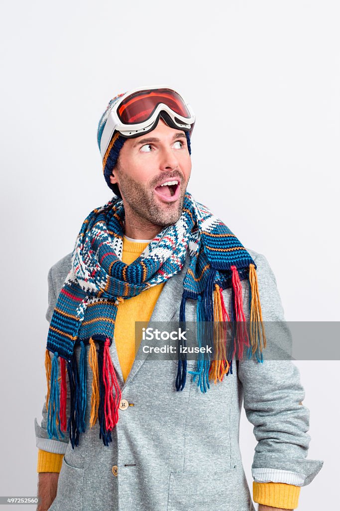 Surprised handsome man in winter outfit Studio portrait of surprised man in winter outfit - cap, scarf and goggles, standing against white background, looking away with mouth open. Men Stock Photo