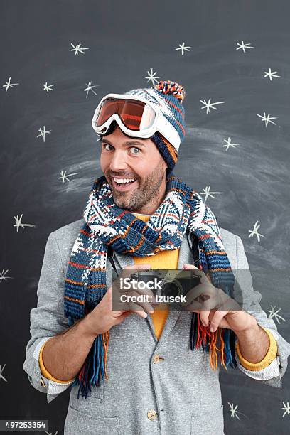 Excited Man In Winter Outfit Against Blackboard Holding A Camera Stock Photo - Download Image Now