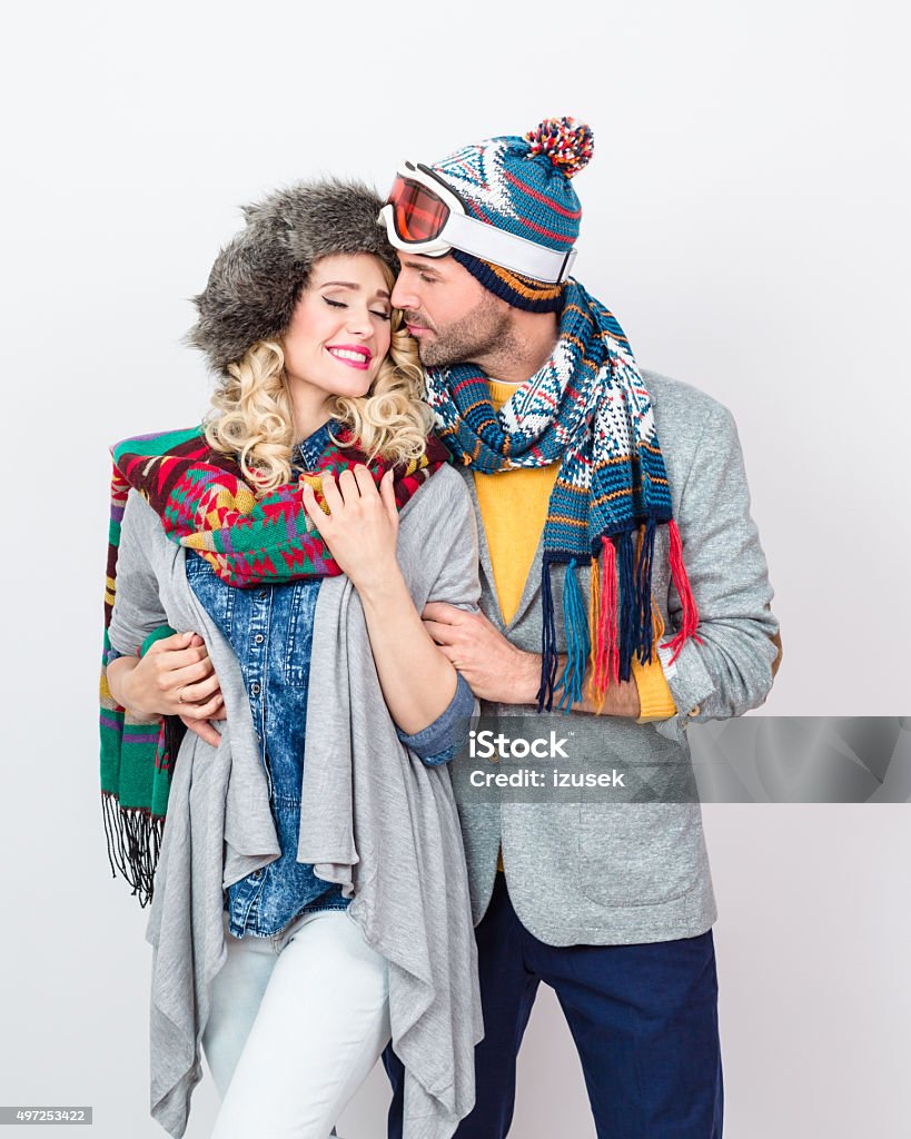 Affectionate couple in winter outfit against white background Studio portrait of happy, affactionate couple in winter outfits - caps, scarfs, sweaters, embracing against white background. Fashion Model Stock Photo