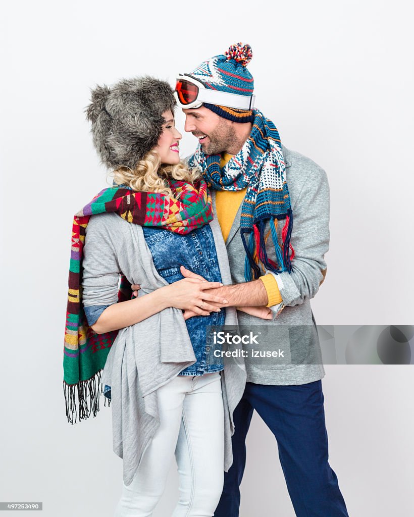 Affectionate couple in winter outfit against white background Studio portrait of happy, affactionate couple in winter outfits - caps, scarfs, sweaters, embracing against white background. Smiling Stock Photo