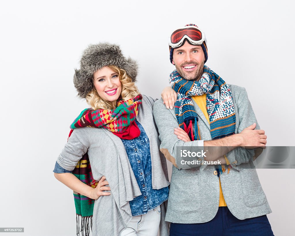 Fashionable, cheerful couple in winter outfit against white background Studio portrait of happy couple in winter outfits - caps, scarfs, sweaters, laughing at camera.  2015 Stock Photo