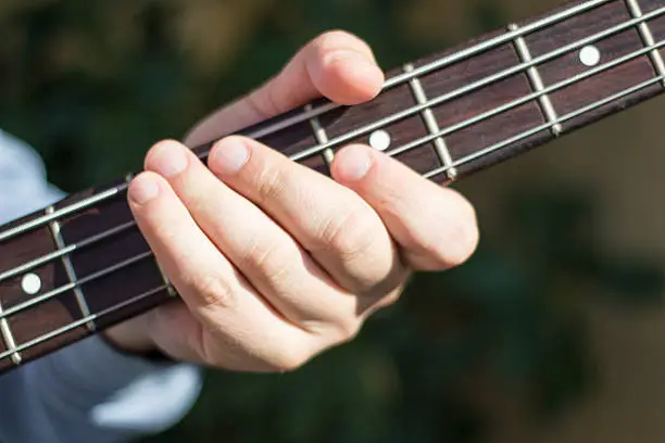 Photo of Fingers on the bass guitar strings. Bass player. Guitar and strings.