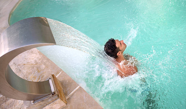 Man relaxing at the spa Handsome woman relaxing at the spa in the swimming pool under a stream of water hydrotherapy stock pictures, royalty-free photos & images