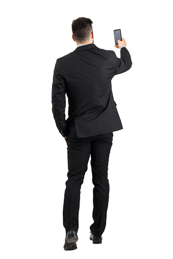 Businessman in suit searching for good phone signal rear view or taking photo. Full body length portrait isolated over white studio background