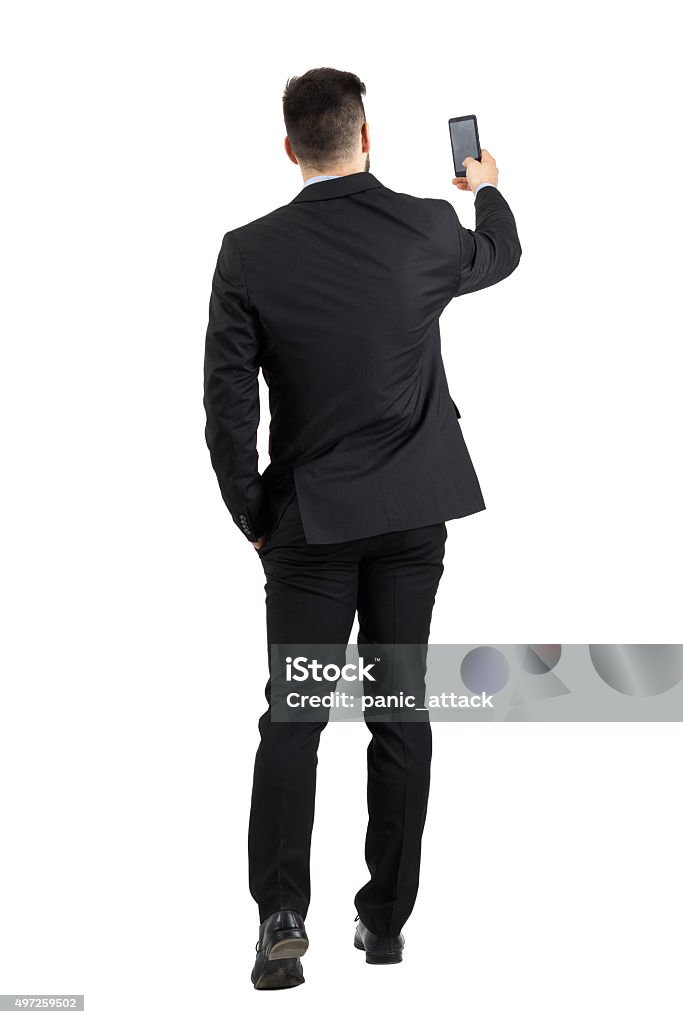 Businessman searching for phone signal rear view or taking photo Businessman in suit searching for good phone signal rear view or taking photo. Full body length portrait isolated over white studio background Rear View Stock Photo