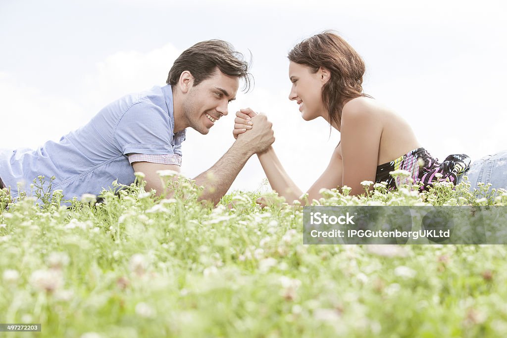 Being in the park Side view of young couple arm wrestling while lying on grass against sky 20-24 Years Stock Photo