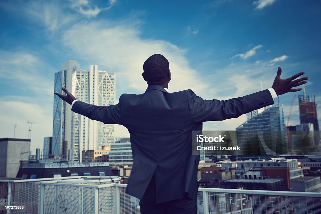 Independence Back view of businessman standing with arms outstretched on the rooftop with the view over the London City. Freedom Stock Photo
