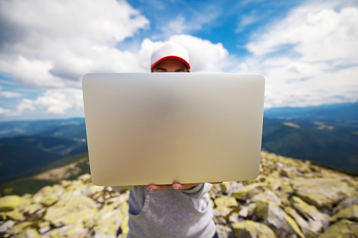 Woman with laptop standing on a stone in the mountain