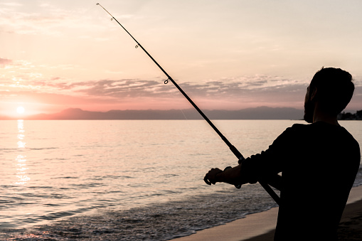 A Fisherman braves the early morning chill of the beach to catch a fish for that day.