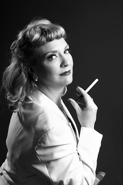Smiling 1940s styled blonde with e-cigarette Vertical B&W studio shot on gray, take-off on glamour cigarette ad. cigarette photos stock pictures, royalty-free photos & images
