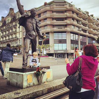 Montreux, Switzerland  - May 8, 2014: Mother photographing her son sitting with Freddie Mercury statue in Montreux. 