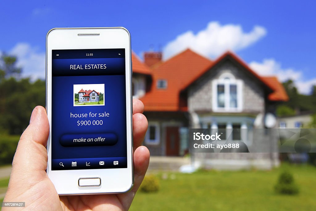 hand holding mobile phone with house sale offer hand holding mobile phone with house sale offer and house as a background Business Stock Photo