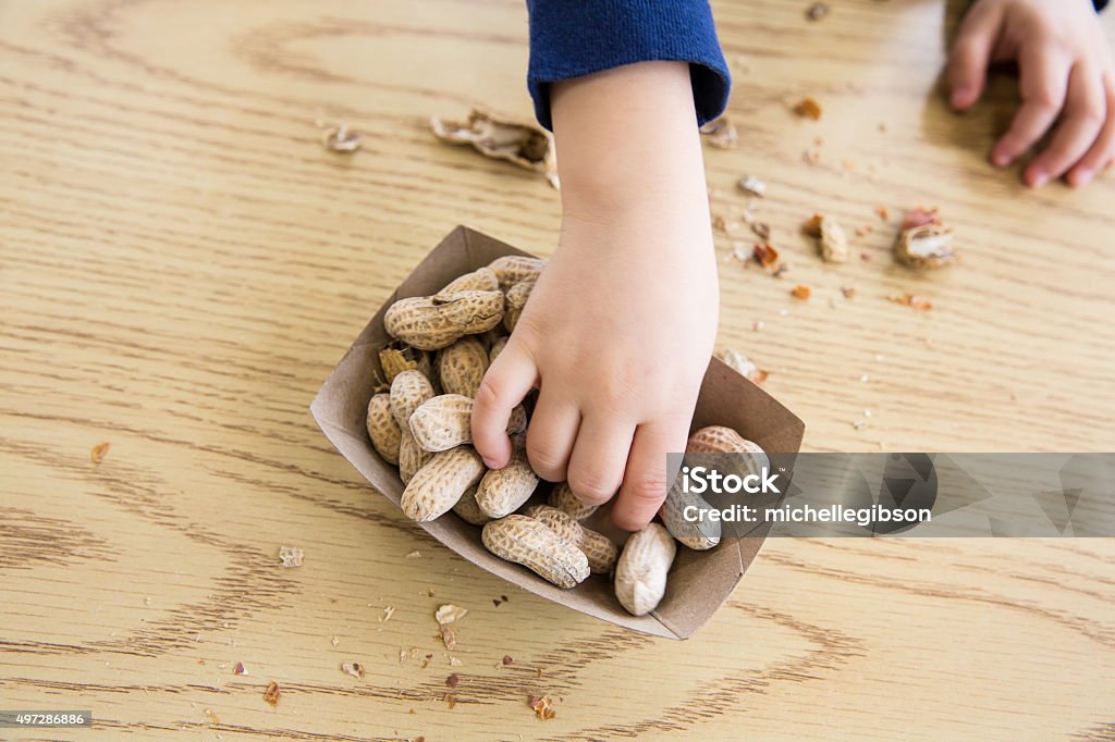 Child eating Peanuts Unrecognizable little boy sits at a table eating peanuts Peanut - Food Stock Photo