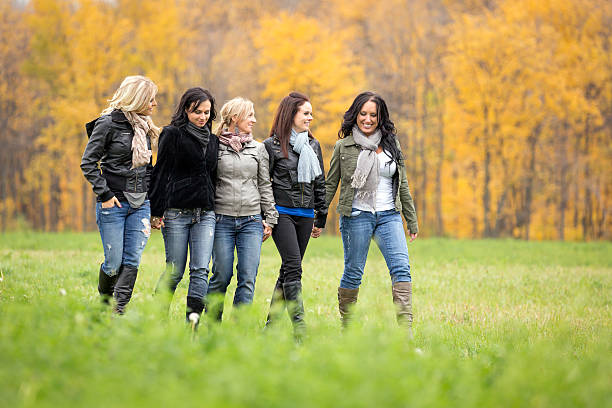 Women friends having fun outdoors walking in a field in autumn season. 