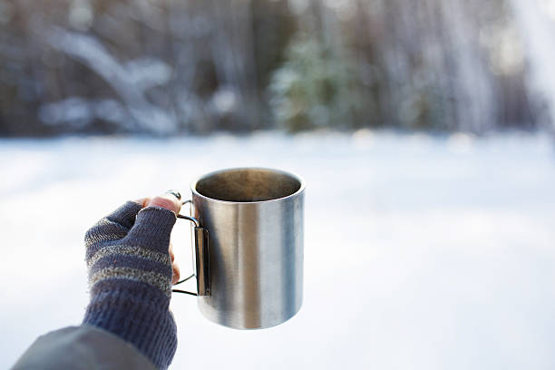 Gloved mitten hand holding a travel mug stock photo