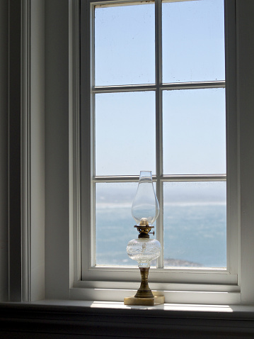 A close-up looking at an Antique Oil Lamp sitting on a window sill in Yaquina Head Lighthouse on the Pacific Ocean in Oregon. This is near the town of Newport, Oregon. This is a historic area from the mid 1800's. The Pacific Ocean is visible in the background.