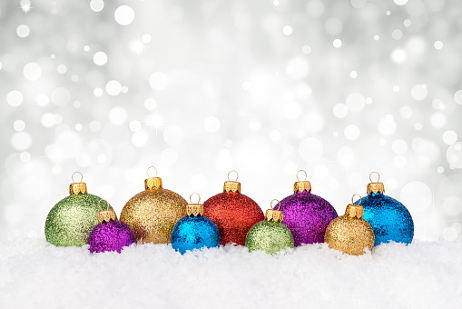 Multicolor decorated big and smal baubles, decorated with glitter lying on snow, nice christmas lights background