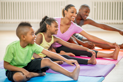 A family is sitting on exercise mats and stretching out their legs during a yoga class.