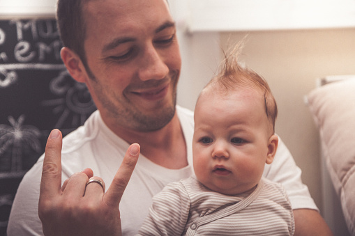 Father showing   his baby girl hand gesturing horns up rock and roll symbol