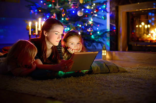 istock Mother and daughters using tablet by a fireplace on Christmas 497315824