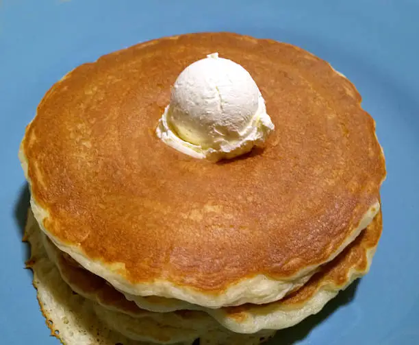 a three stack of pancakes with butter on top.