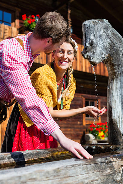 paar in der berghütte trinkwasser aus source - österreich tracht stock-fotos und bilder