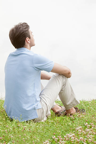 istock Rear view of thoughtful young man sitting on grass 497341655