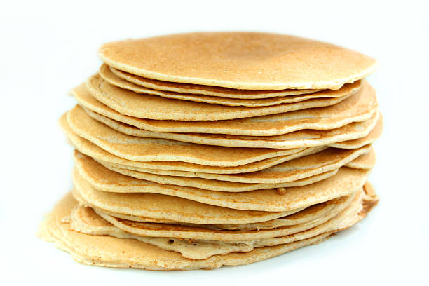 Blurred Caucasian redhead woman flips a pancake with a spatula on the electric skillet, her defocused daughter watching the cooking process in the sunny kitchen. Focus on a pancake on electric pan