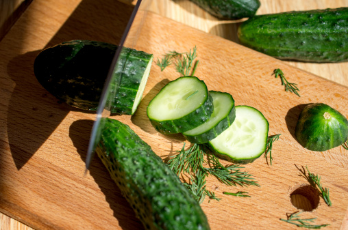 Cucumbers cut knife on a wooden board and dill.