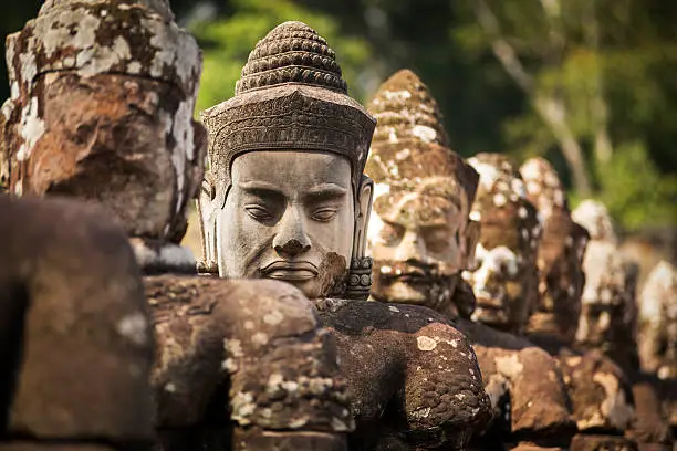In a row, a newly made Buddhist head stands out from the other ancient statues. Situated along the road leading to the gate of Angkor Thom temple, there has been substantial renovation work in Angkor Wat UNESCO Heritage site. Selective focus on the new stone head.