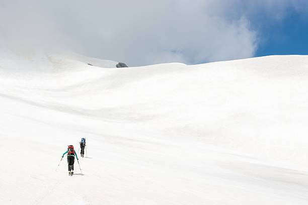 Skiiers ascending mountain slope stock photo