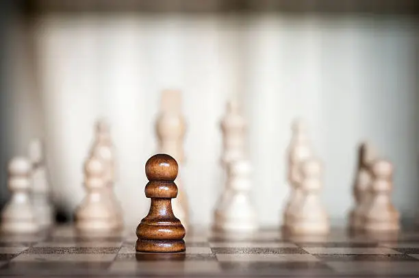 Lone Black Chess Pawn With Multiple White Chess Pieces In The Background