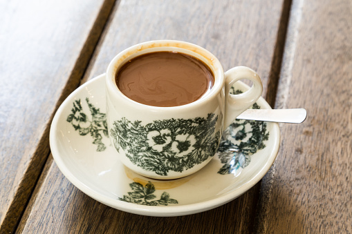 Traditional oriental Chinese coffee in vintage mug and saucer on wooden table in soft focus setting with ambient light